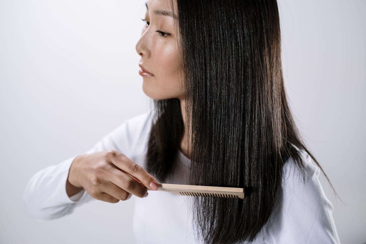 Studio portrait of an Asian woman combing her straight black hair indoors with a white background.